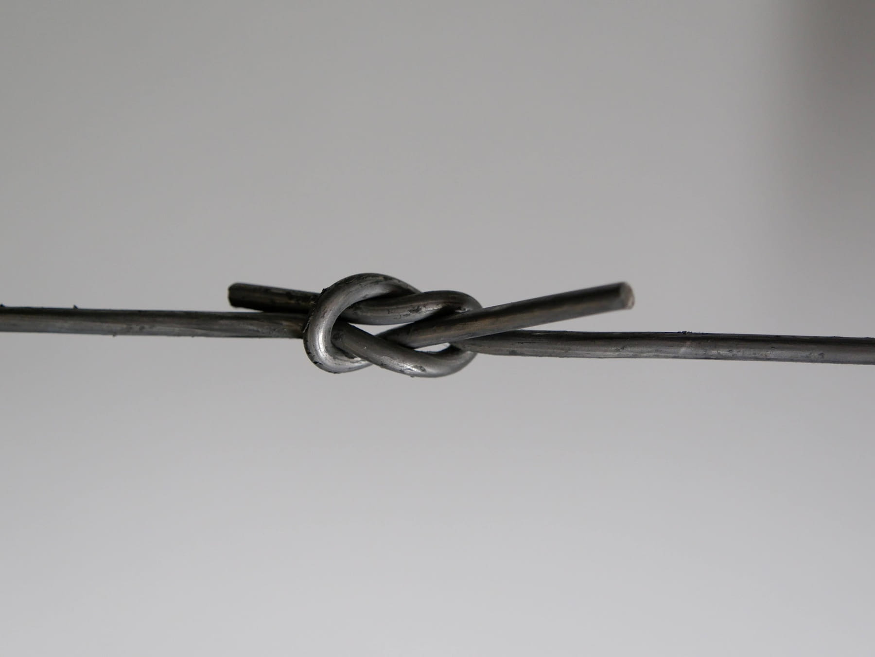 Baling wire tied in a flat reef knot, showing ductility under load